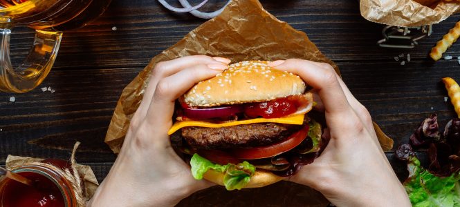 Barbequed Maple Balsamic Burgers – Harvest Grilling Series Hands holding fresh delicious burgers with french fries, sauce and beer on the wooden table top view.