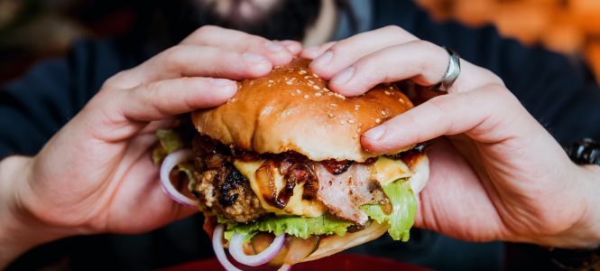 Baby, That’s a Good Merlot Onion Burger! – Winter Game Day Series Young man eating a cheeseburger. Restaurant